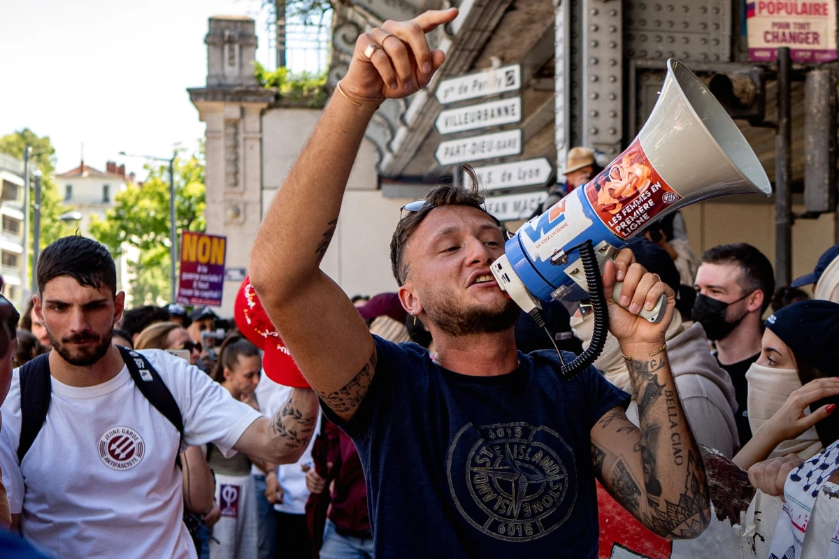 Gros plan d’un homme masqué de La Jeune Garde tenant une banderole lors d’une manifestation en rue