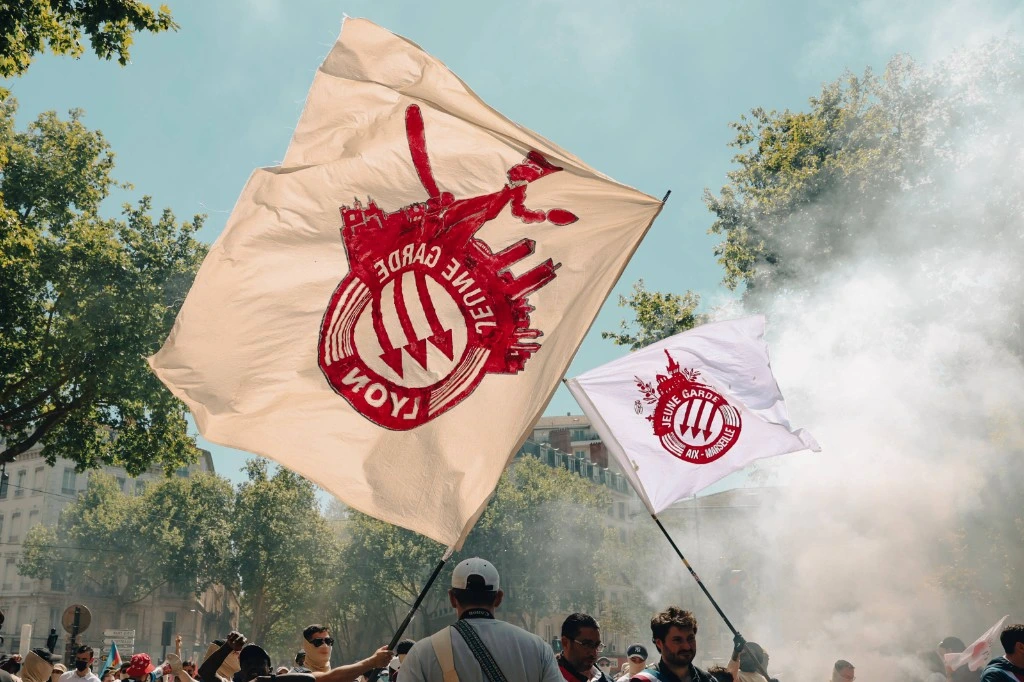 Le gouvernement saisit la justice sur Jeune Garde, foule et drapeaux devant un bâtiment officiel.