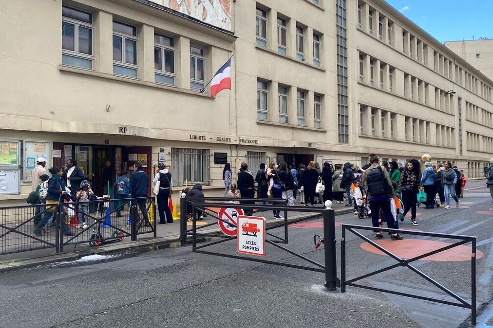 Animateur d’école à Paris escorté par des policiers devant une école, ruban de sécurité en arrière-plan