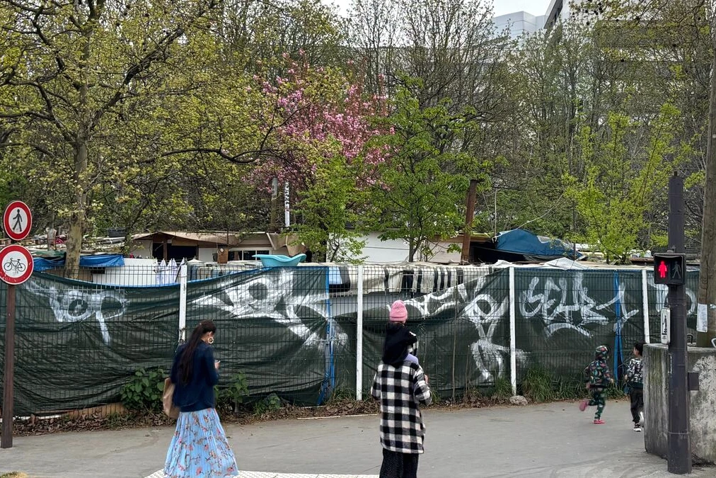 Bidonville à la porte d’Aubervilliers : tentes et cabanes alignées près d’un grillage, immeubles au fond