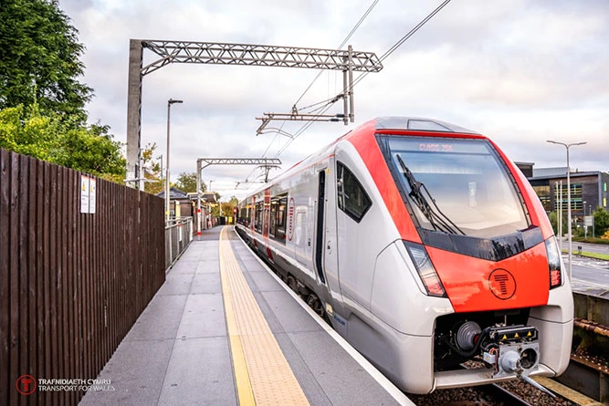 Billets de train Transport for Wales affichés sur un écran, avec un train en arrière-plan en gare