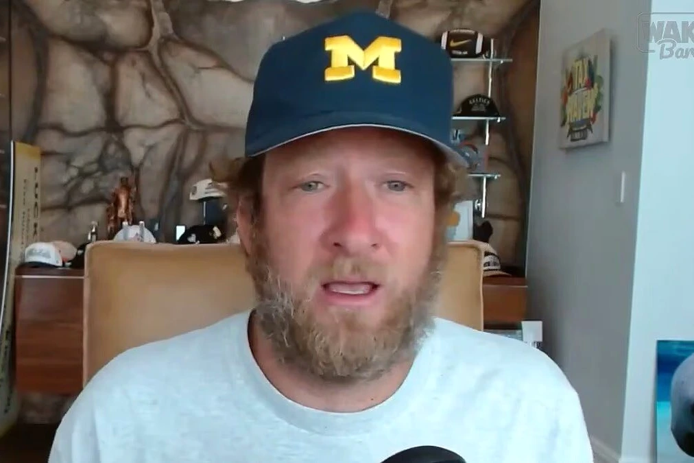 Dave Portnoy s’exprime face caméra, avec une photo de Tiger Woods et une voiture de police en arrière-plan