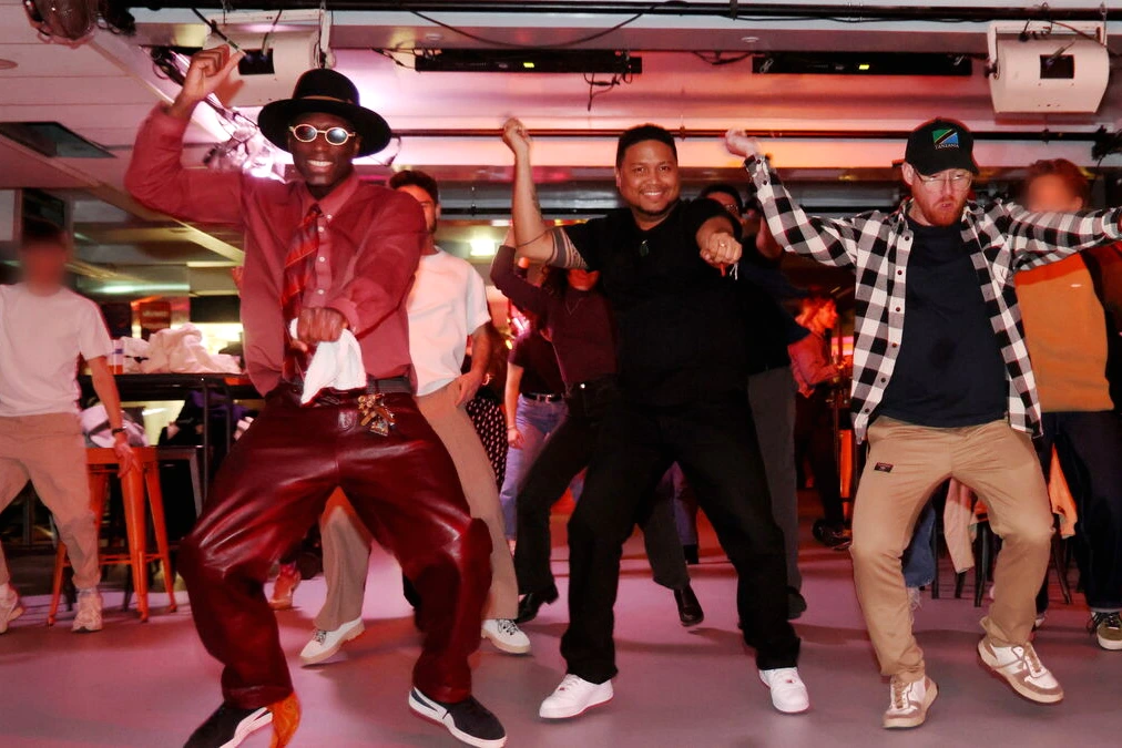 Des anonymes mettent l’ambiance dans un bar parisien, verres levés et foule souriante autour du comptoir