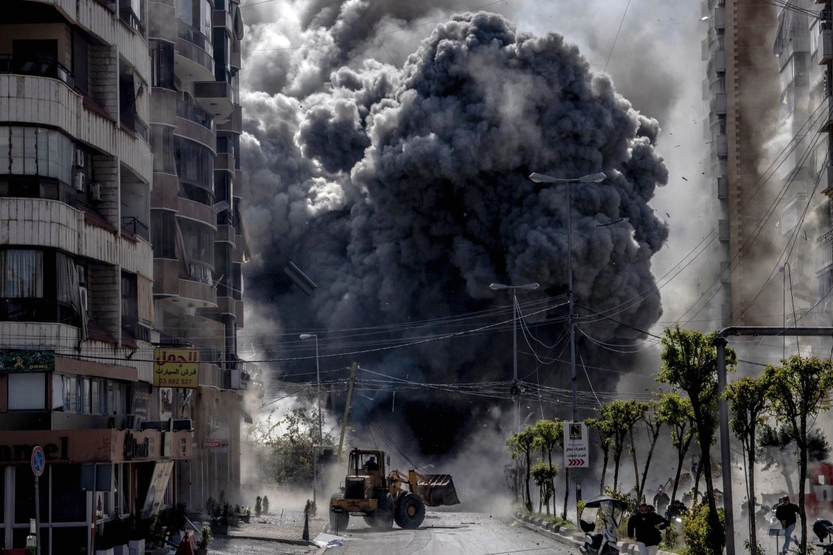 Drapeau libanais flottant devant des immeubles endommagés, avec fumée au loin dans le ciel gris
