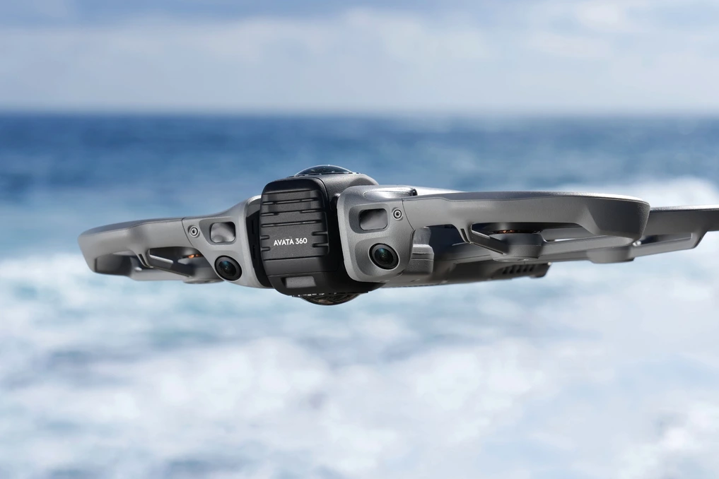 Drone DJI Avata 360 en vol, avec caméra 360° visible, sur fond de ciel bleu et paysage urbain