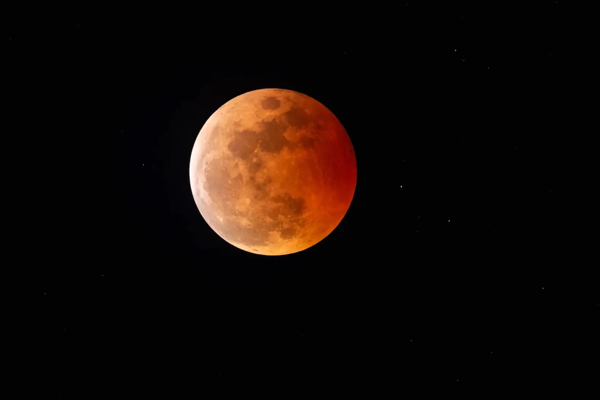 Éclipse lunaire totale : la Lune rouge sombre partiellement voilée par des nuages dans un ciel nocturne