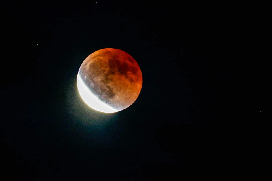 Éclipse totale de la Lune : disque rougeâtre dans un ciel nocturne sombre, légèrement voilé de nuages