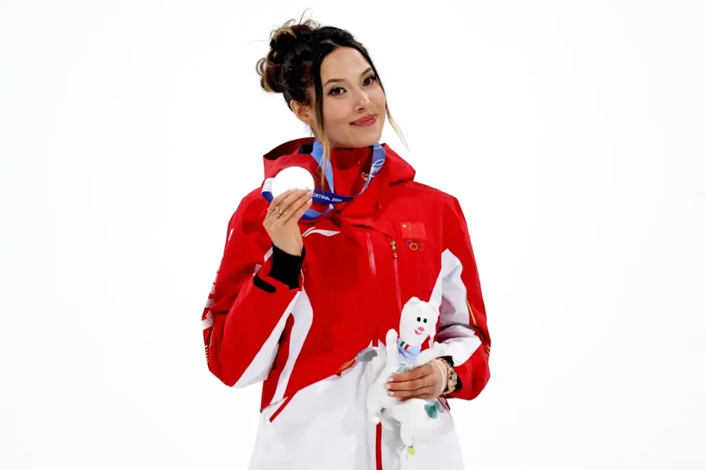 Eileen Gu souriante, saluant le public lors d’un défilé à San Francisco, sous les projecteurs.