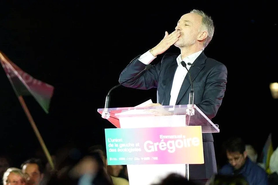 Emmanuel Grégoire en costume, parlant devant l’Hôtel de Ville de Paris, avec voitures en arrière-plan