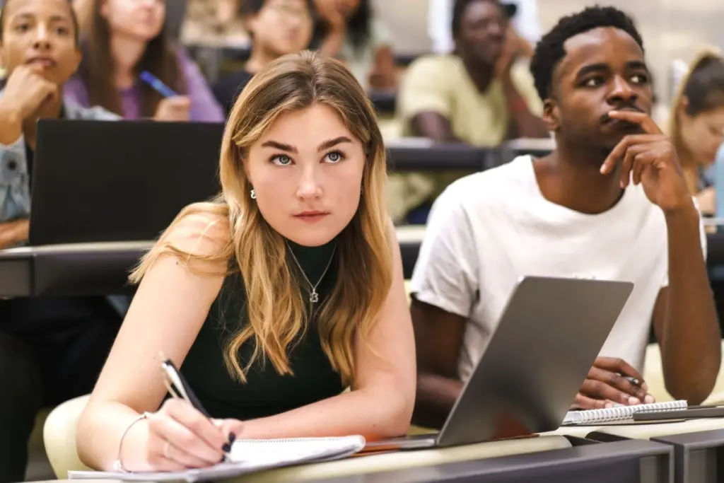 Étudiant à l’université utilisant une IA sur ordinateur portable, entouré de livres et notes sur un bureau