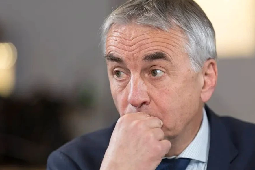 Jean-Luc Rigaut devant la mairie d’Annecy, en costume, avec le bâtiment et des passants en arrière-plan