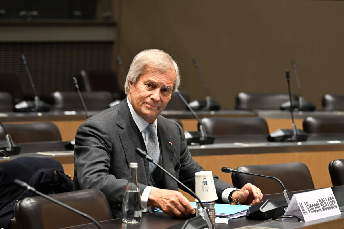 Logo du groupe Bolloré sur un immeuble, avec un écran affichant une interface d’IA en arrière-plan