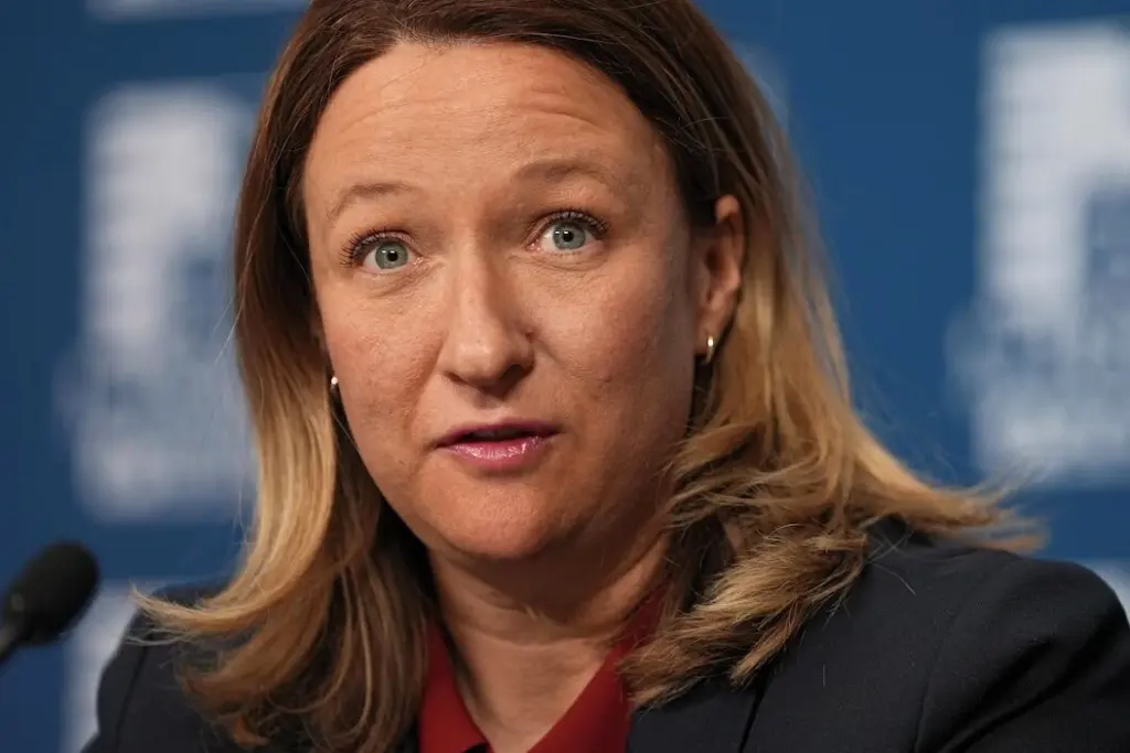 Maïté Blanchette Vézina au pupitre lors d’une conférence de presse, micros et drapeaux en arrière-plan