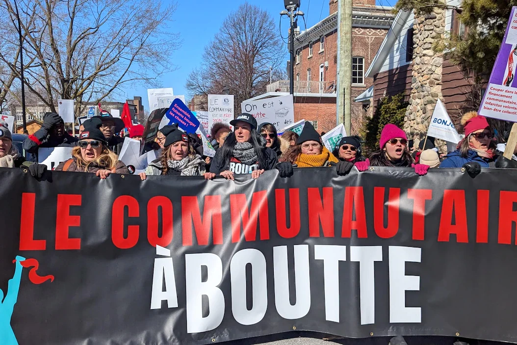 Manifestants du communautaire à boutte devant l’hôtel de ville de Longueuil, pancartes et drapeaux levés