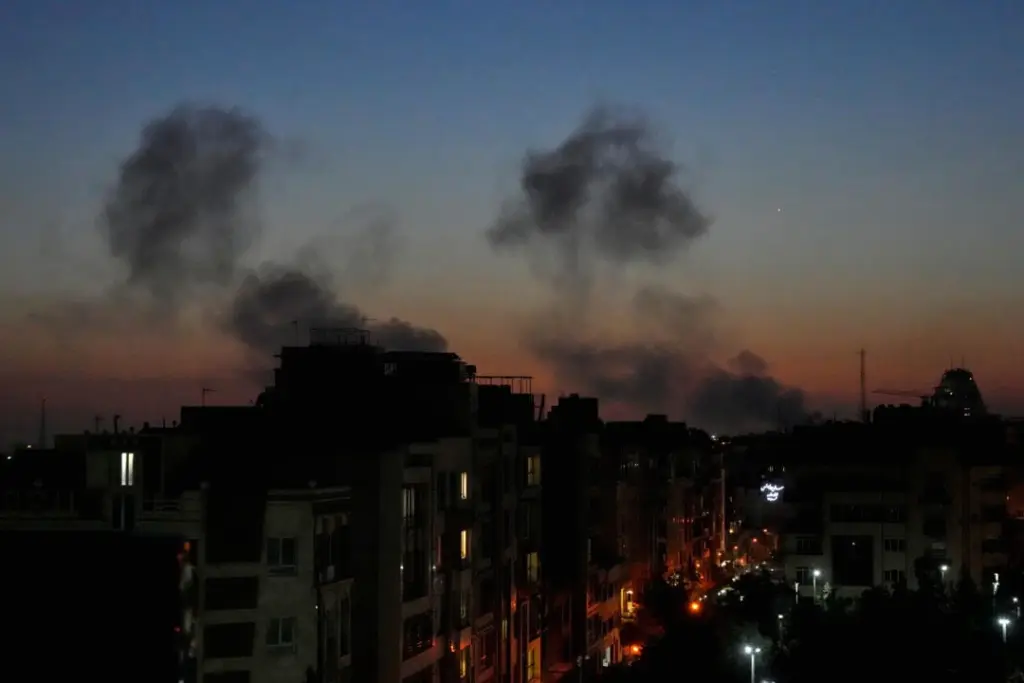 Panache de fumée au-dessus de Téhéran après des frappes israéliennes, immeubles en silhouette au crépuscule