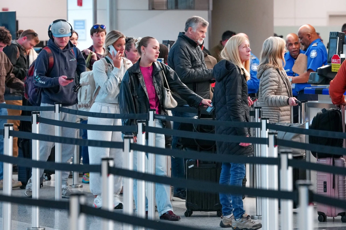 Passagers TSA contrôlant des voyageurs à un poste de sécurité d’aéroport américain, vols perturbés en arrière-plan