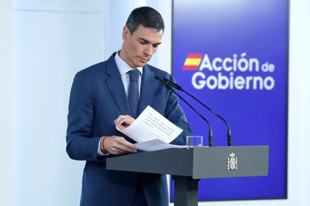 Pedro Sánchez au pupitre, en costume, parlant devant des drapeaux espagnols et européens, en conférence de presse