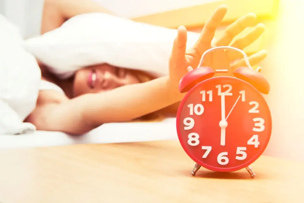 Personne dormant paisiblement dans un lit, réveil analogique sur la table après le changement d’heure