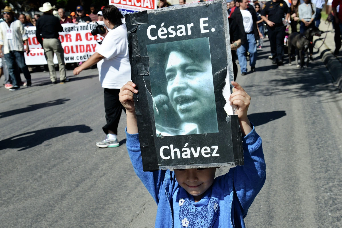 Portrait de César Chávez en noir et blanc, affiché sur une pancarte tenue lors d’un rassemblement.