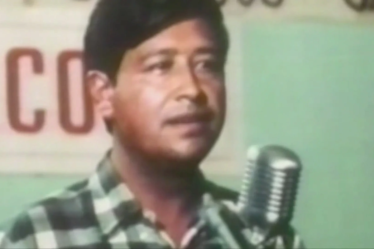 Portrait de Cesar Chavez sur une affiche, devant une école de Fresno avec panneaux et drapeaux en arrière-plan