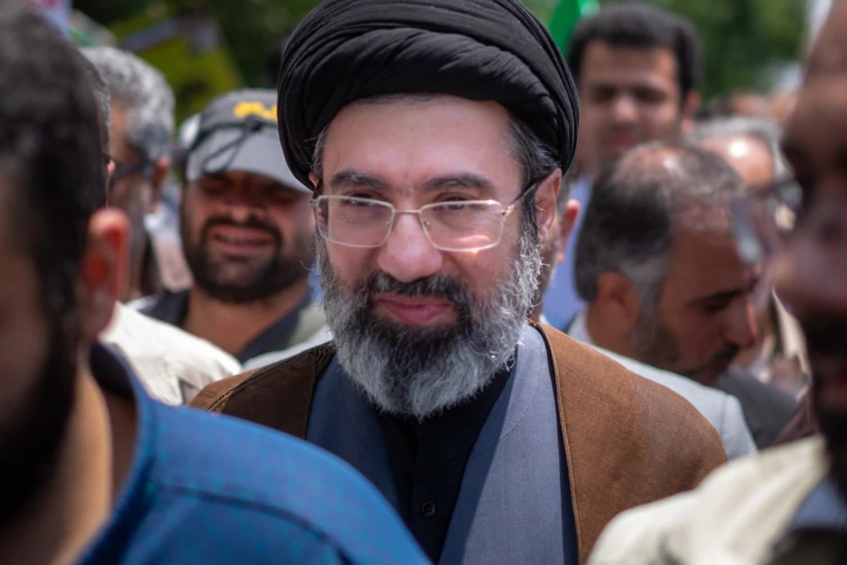 Portrait de Mojtaba Khamenei en tenue sombre, devant un fond neutre, regard tourné vers la caméra