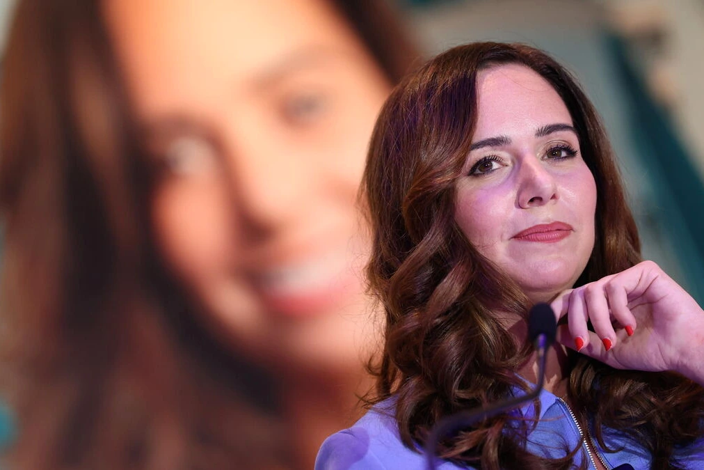 Sarah Knafo au pupitre lors d’un meeting, micro devant elle, drapeaux et foule en arrière-plan