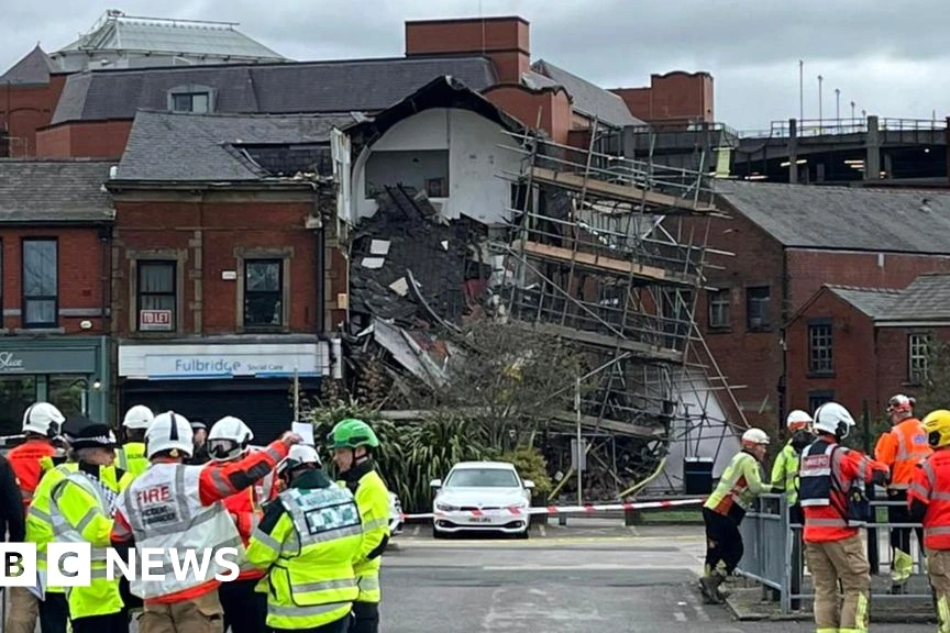Secouristes et pompiers devant un bâtiment effondré à Oldham, décombres et rubalise visibles