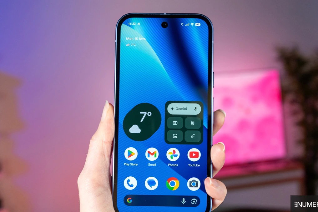Smartphone Android 17 affichant l’écran d’accueil, avec logo Google en arrière-plan sur fond coloré