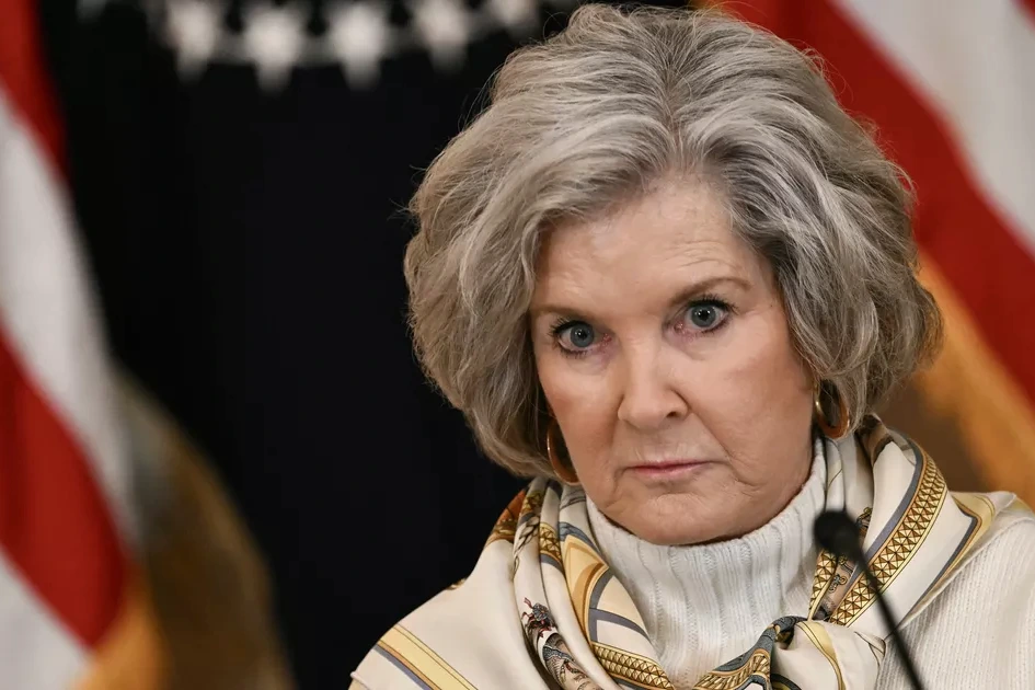 Susie Wiles posant devant des drapeaux américains, en tailleur, lors d’un événement politique aux États-Unis