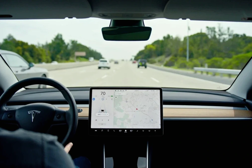 Tesla sur une route européenne, écran de conduite autonome visible, panneaux routiers et voitures en arrière-plan