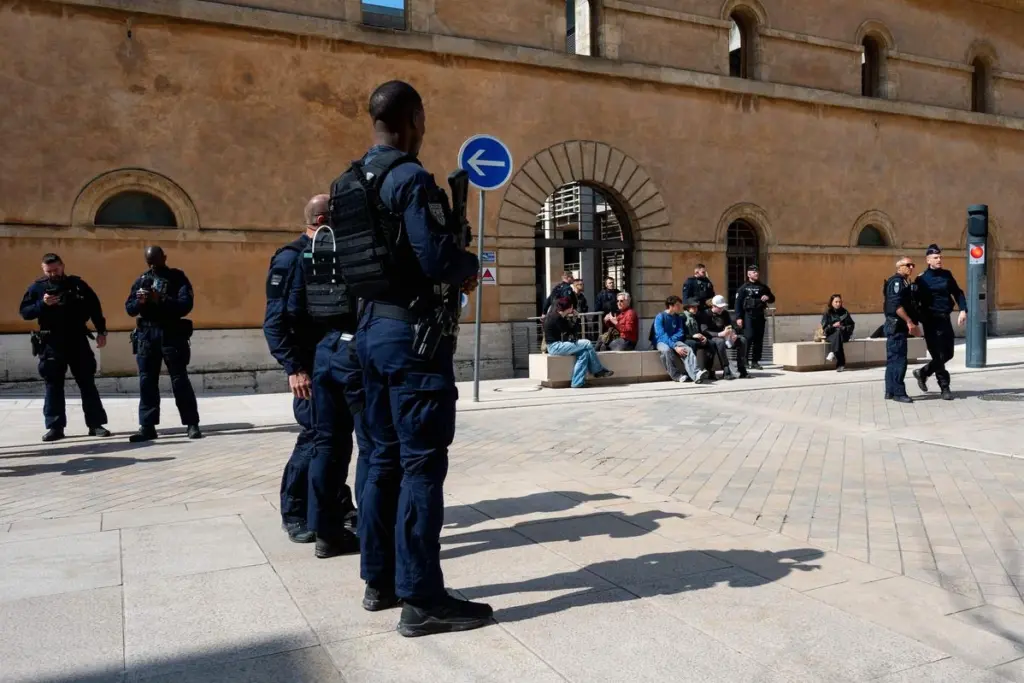 Un policier encadre un homme menotté au tribunal lors du procès de la DZ mafia, journalistes en arrière-plan
