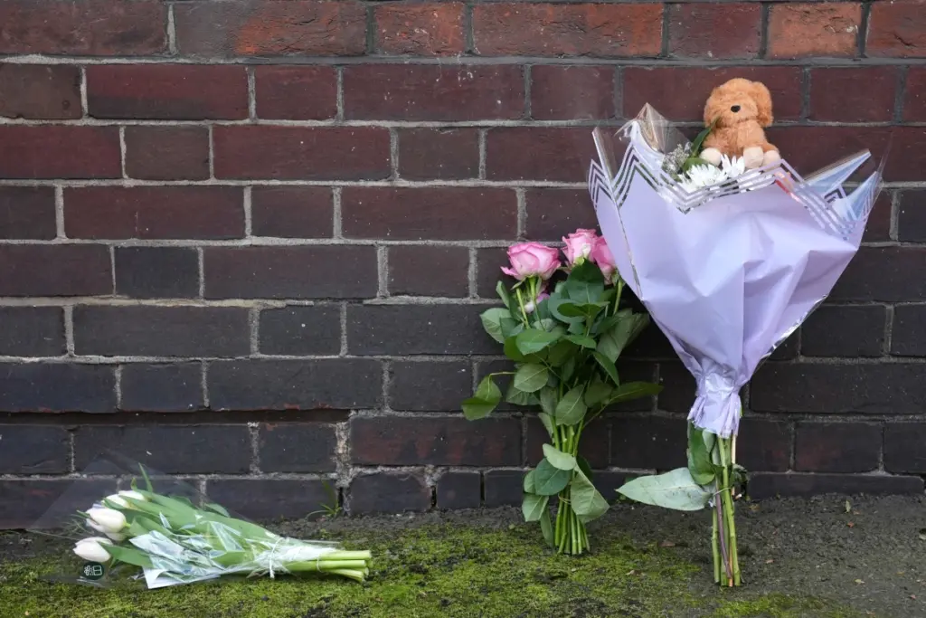 Une mère menottée escortée par la police, tandis qu’un bébé est transporté sur une civière en arrière-plan.