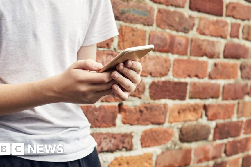 Adolescent de moins de 16 ans tenant un smartphone, icônes de réseaux sociaux floutées à l’écran