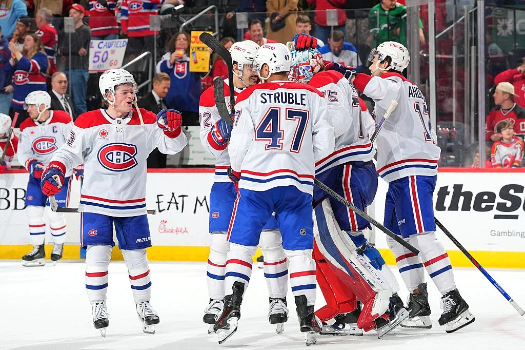 Cole Caufield en uniforme des Canadiens, patinant avec la rondelle et levant la tête vers le filet