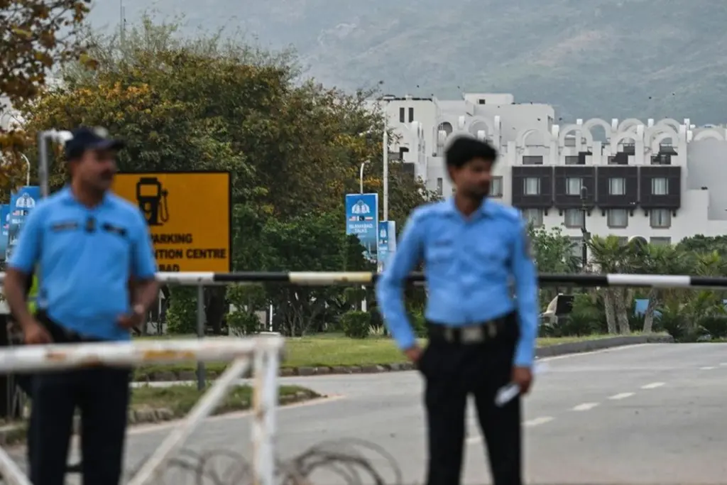Drapeaux de l’Iran et des États-Unis côte à côte devant une table de négociation et des microphones