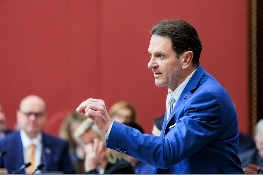 Fréchette en point de presse, debout au micro devant des journalistes, avec Bonnardel en arrière-plan