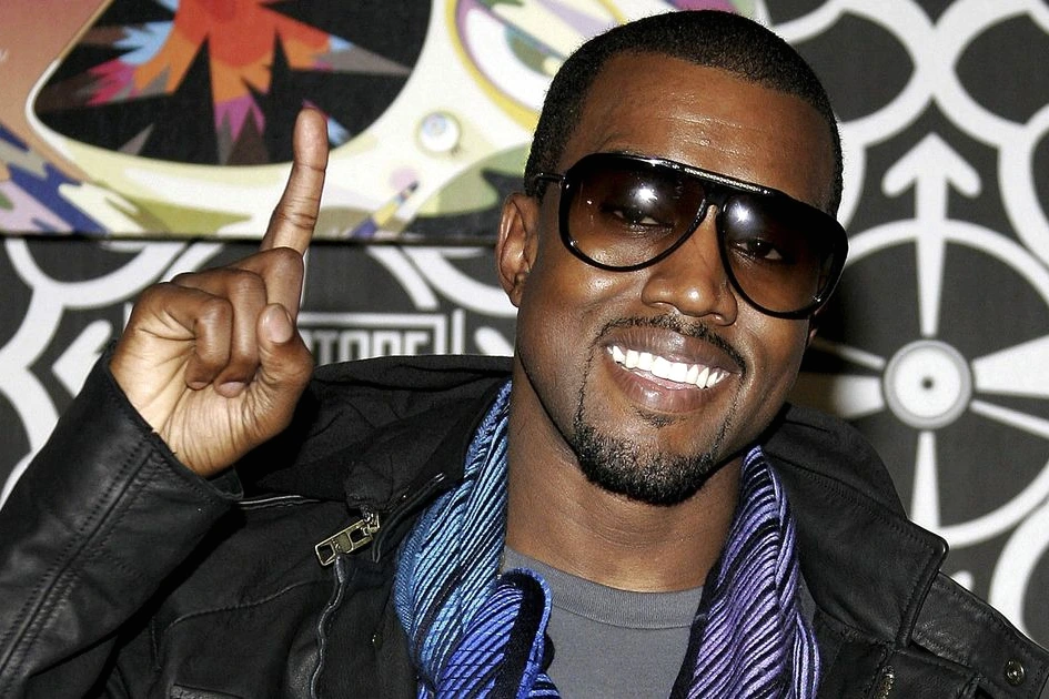 Kanye West sur scène avec micro, éclairé par des projecteurs, devant une foule lors d’un concert.