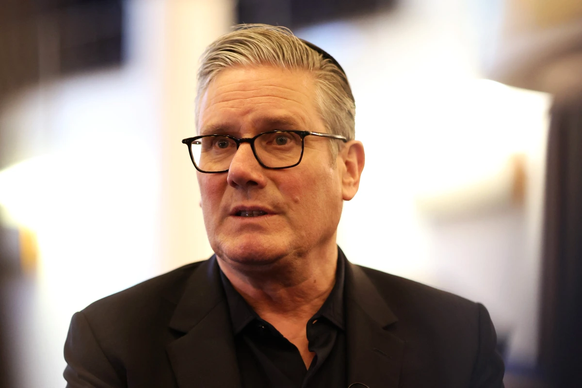 Keir Starmer en costume sombre, debout devant des drapeaux britanniques lors d’une conférence de presse.