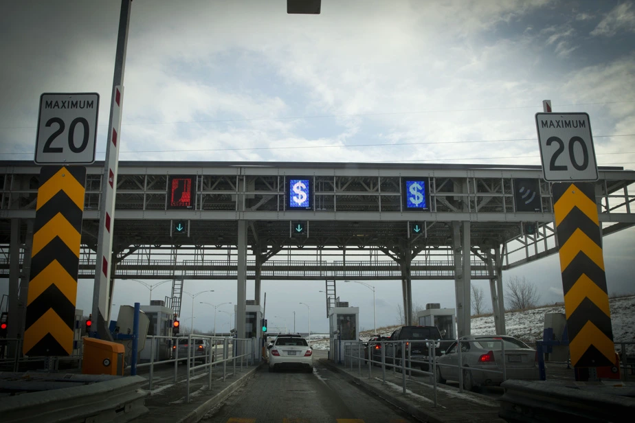 Le ministre des Transports s’exprime au micro lors d’un point de presse, avec panneaux de péage en arrière-plan