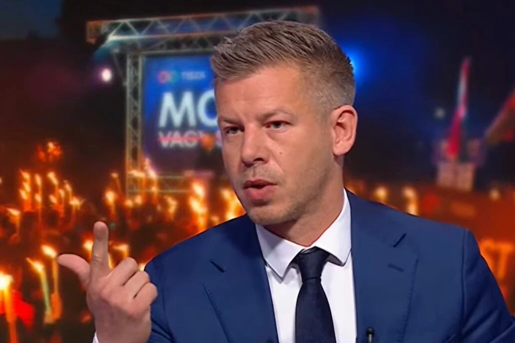 Logo de Magyar sur fond de drapeau hongrois, avec microphones et caméras devant un bâtiment public à Budapest