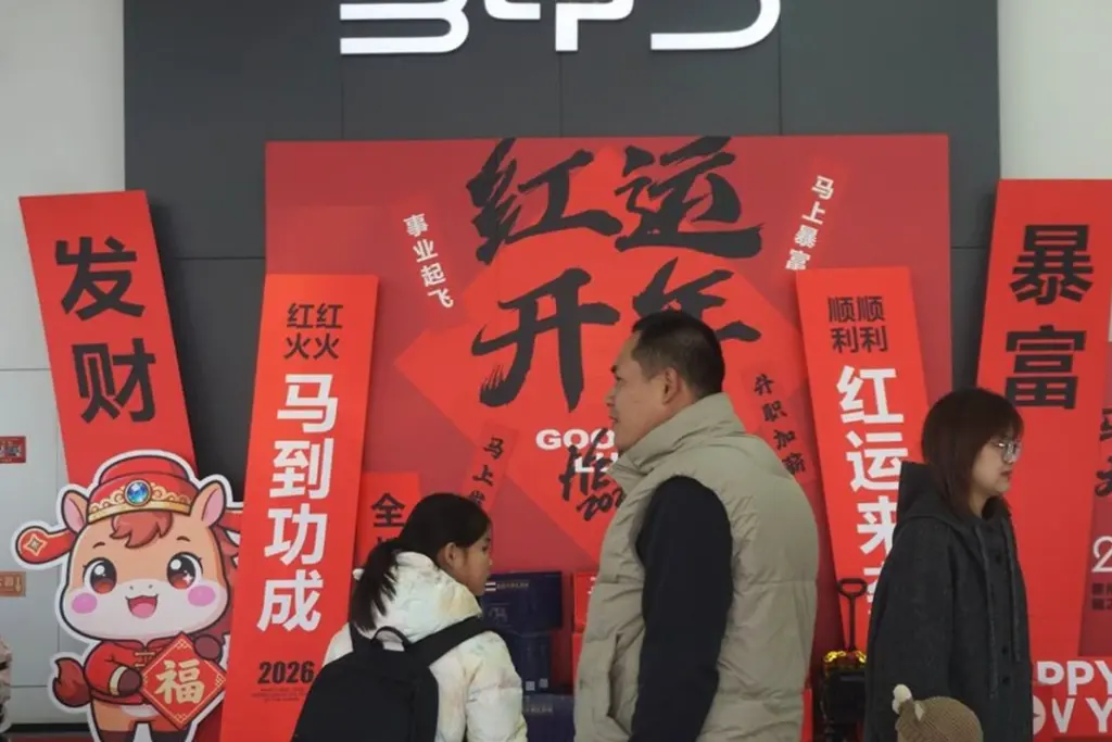 Logo Tesla sur une voiture électrique, avec en arrière-plan un panneau BYD dans une concession en Europe