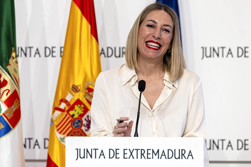 María Guardiola au pupitre, entourée de membres du gouvernement, avec le logo Vox en arrière-plan