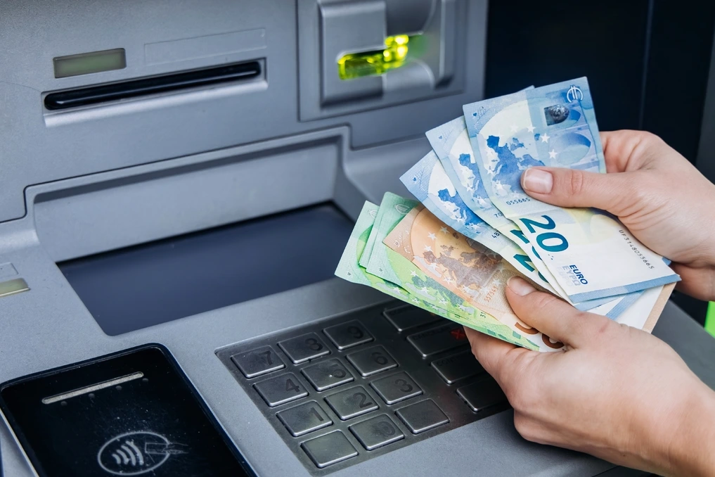 Personne retirant des espèces à un distributeur automatique en France, sans carte bancaire, avec smartphone en main