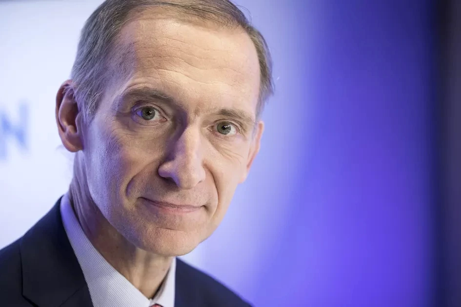 Portrait de Nicolas Baverez en costume, devant un fond sombre avec des motifs numériques lumineux.