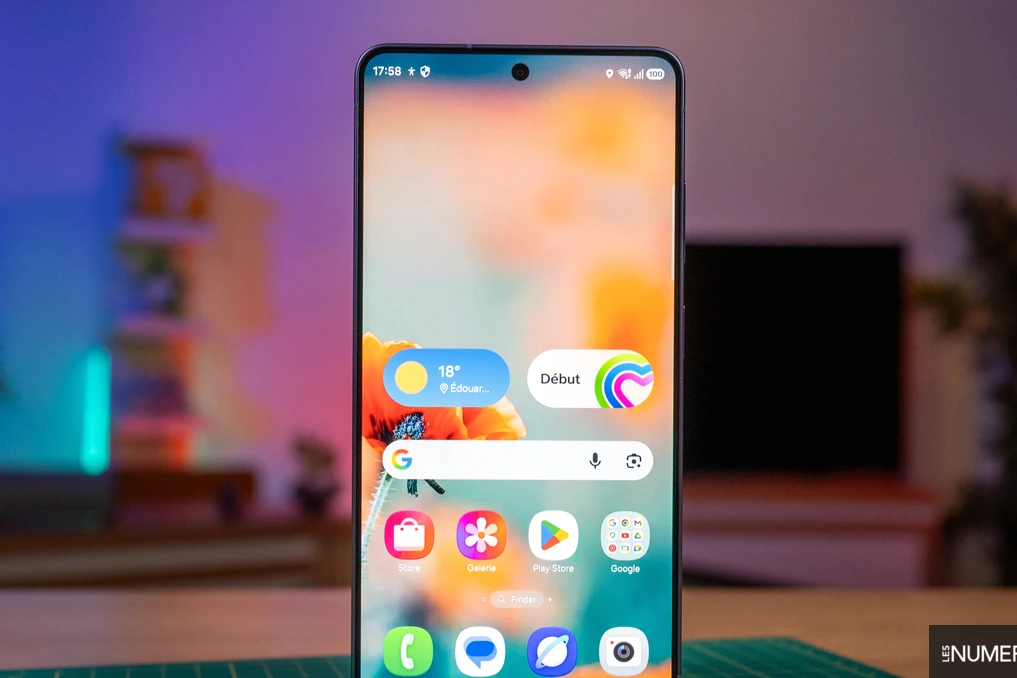 Samsung Galaxy S26 tenu en main, écran allumé, avec icônes d’alerte et réglages ouverts en arrière-plan