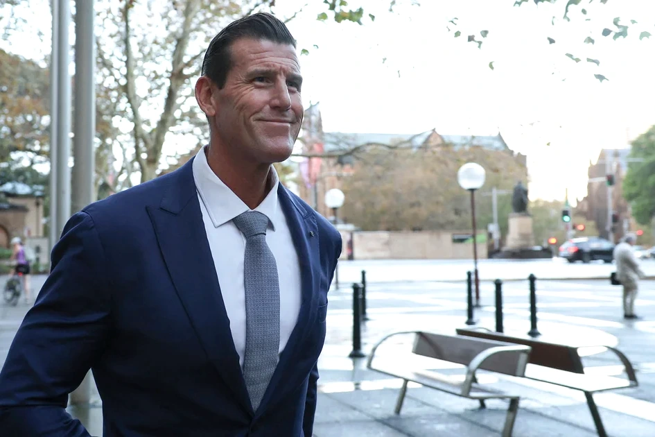 Soldat australien décoré en uniforme, vu de profil, devant des drapeaux, en conférence de presse.