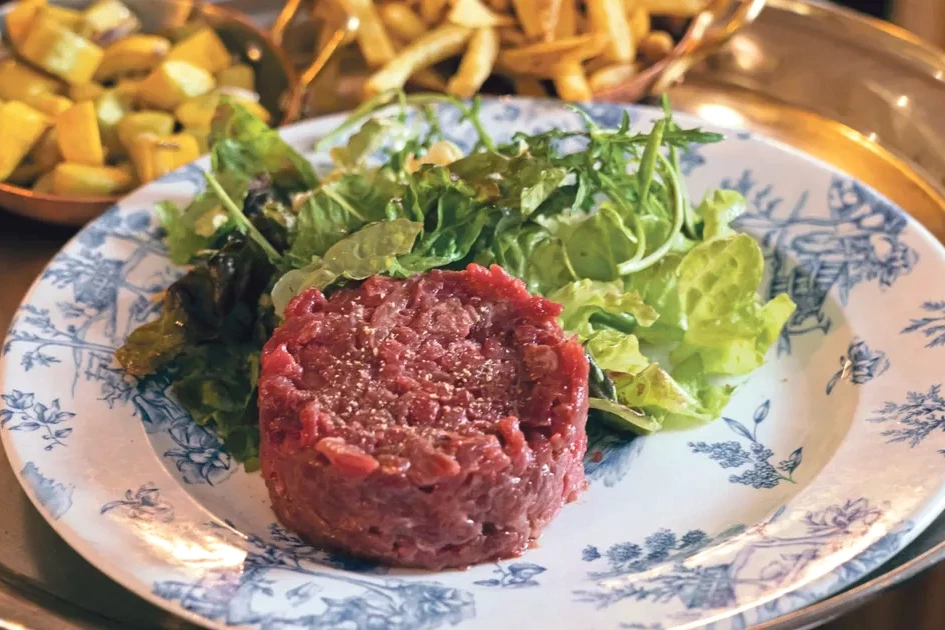 Tartare de bœuf à Paris servi dans une assiette, avec frites dorées et salade, sur table de bistrot.