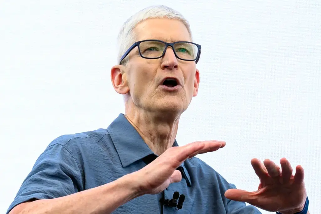 Tim Cook sur scène devant un grand logo Apple, en costume, s’adressant au public lors d’une keynote.