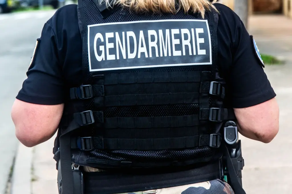 Un enfant de 9 ans assis sur un lit dans une pièce sombre, tandis que son père est escorté par des policiers.