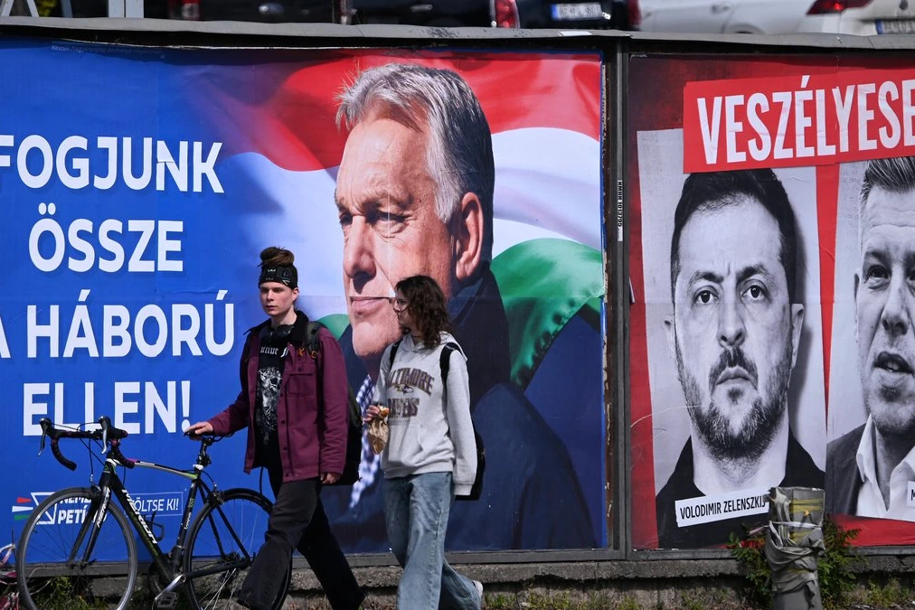 Viktor Orbán s’exprime au pupitre lors d’un meeting en Hongrie, drapeaux hongrois en arrière-plan.
